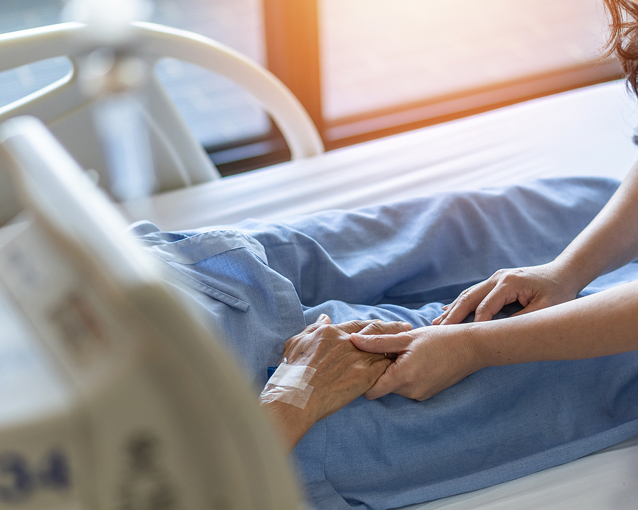 Medical personnel holding a patient's hand in a hospital bed.