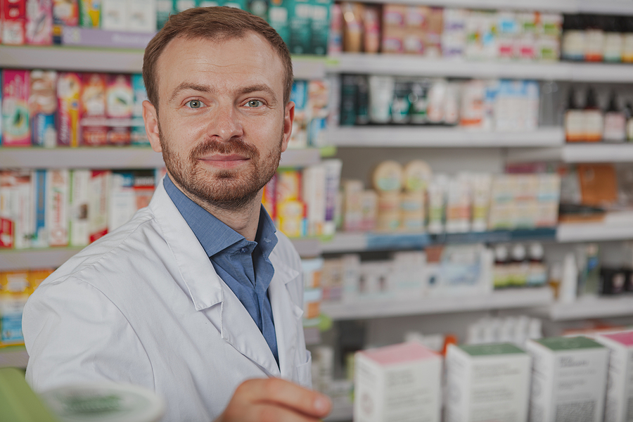 Pharmacist working in a busy pharmacy, smiling and looking at the camera.