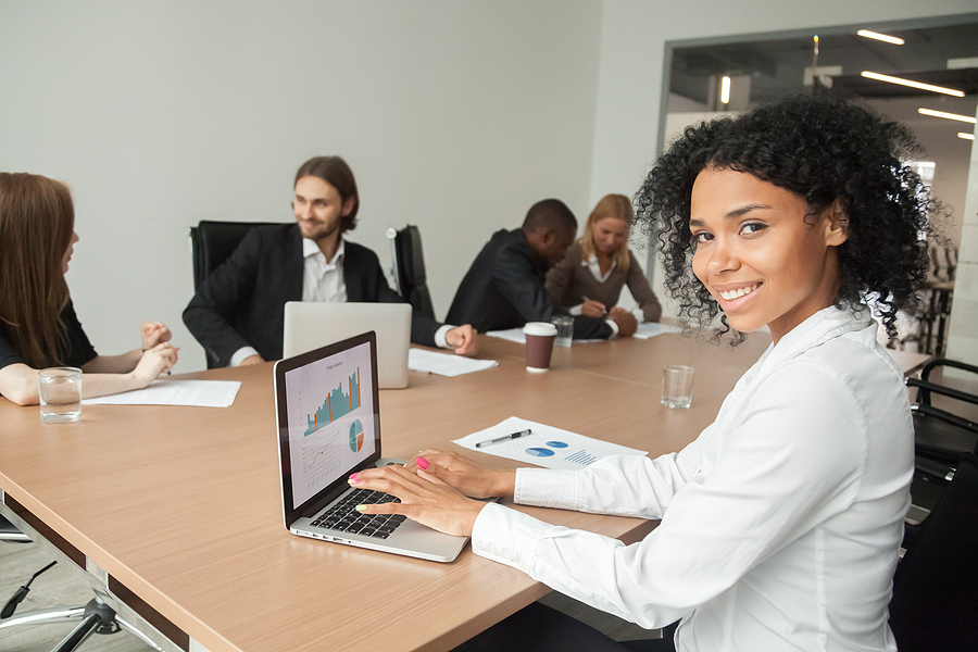 Smiling hospital administrator sitting at a conference table with her laptop open to a report.