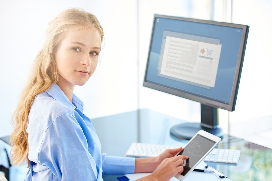 Administrator sitting at a desk in front of a computer holding a tablet.