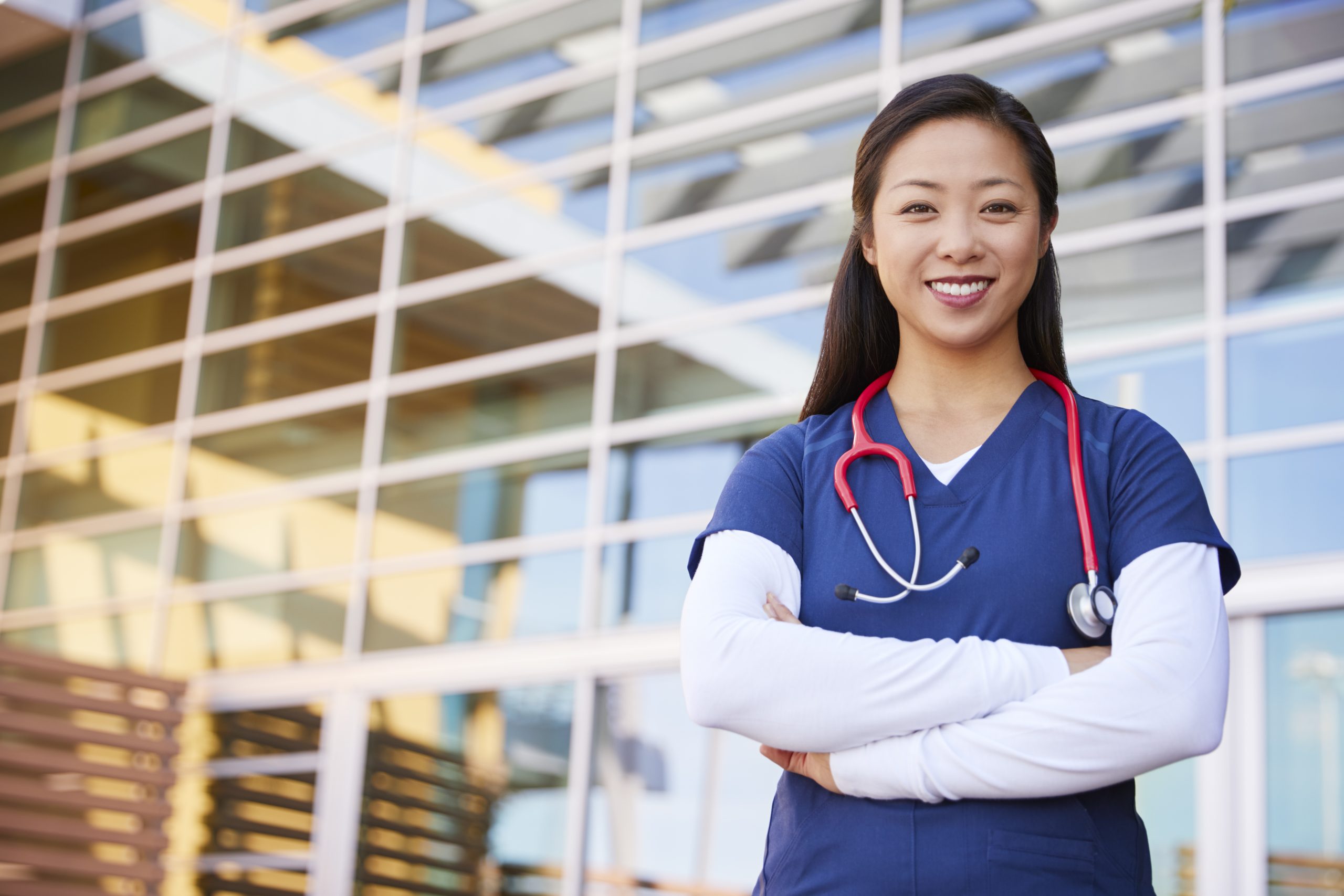 Smiling female healthcare worker wearing scrubs standing in a hospital.